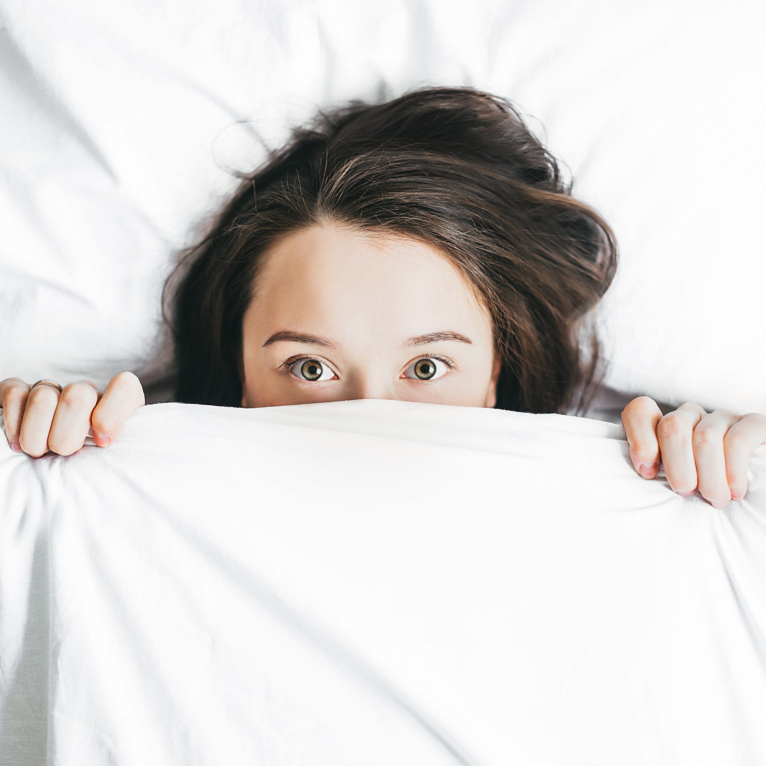 woman poking head out from under covers in bed