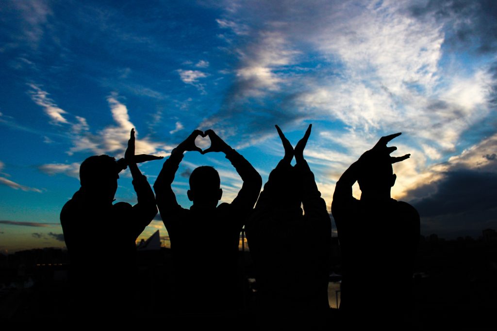 four people spelling LOVE with their hands against a blue sky
